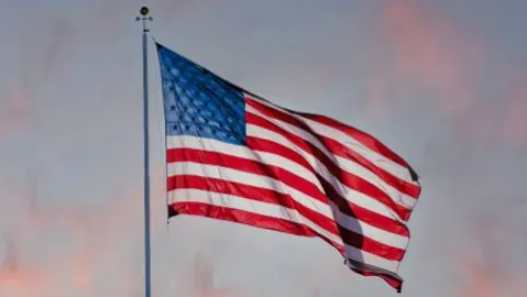 An American flag blowing in the wind with a blue sky in the background.