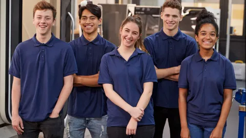 Young apprentices in blue shirts smile for the camera