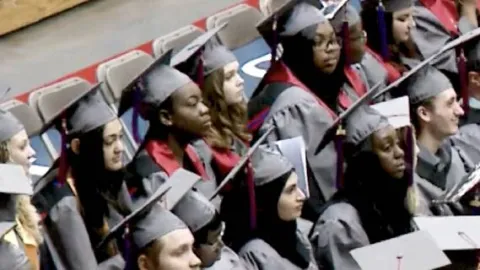 A group of Brookdale Community College students wearing a black cap and gown are seated at a graduation ceremony.
