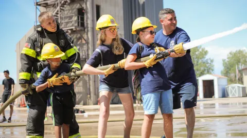 Middle school kids with hardhats shoot water out of a fire hose with help from real firefighters