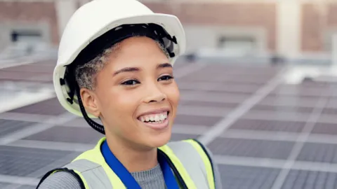 Young black woman with hardhat walks around a field of solar panels