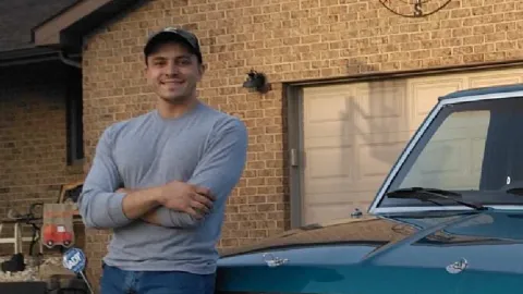 Austin Kolas, a Cummins technician, stands in his driveway, leaning up against his turquoise Ford Ranger truck. 