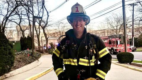 Jeffrey Kaplan, firefighter ambassador, stands in front of a firetruck in his gear