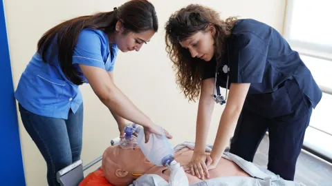 Two nursing students learn how to save real patients by practicing CPR on a dummy in a healthcare setting