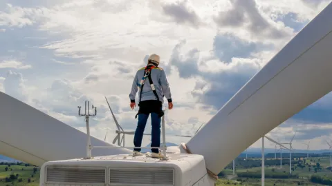 Wind turbine technician stands on the nacelle at the top of a wind turbine