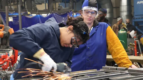 two women in jumpsuits practice their welds in trade school class