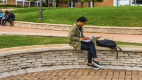 A student sits outside on a ledge on the Triton College campus.