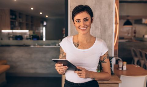 Young female food service manager with tattoos holding a tablet in a restaurant