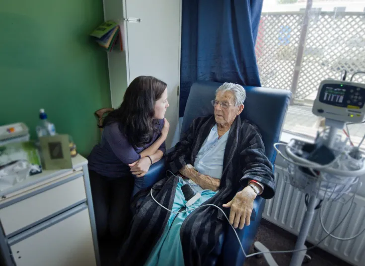 A social services assistant checks on an elderly client in a medical setting