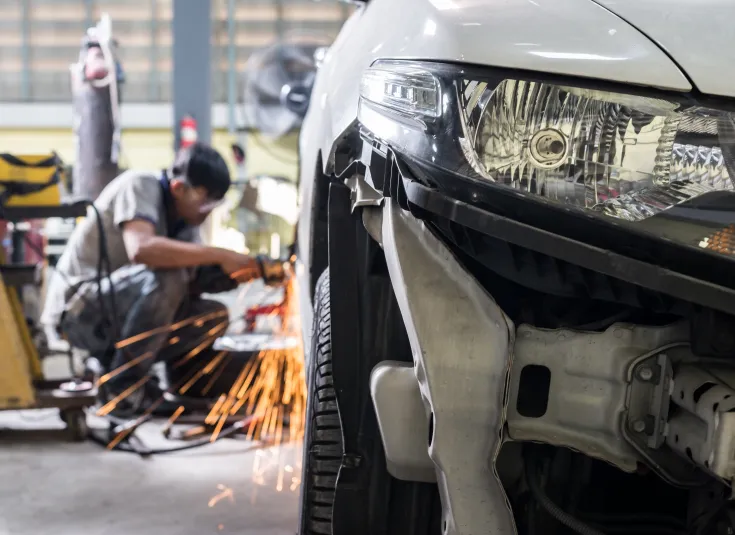 Auto body technician uses a grinder to repair a vehicle