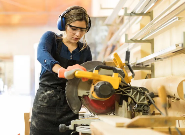 A female carpenter uses a miter saw to cut a piece of wood in the shop
