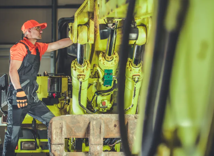 A heavy equipment mechanic inspects a broken excavator arm