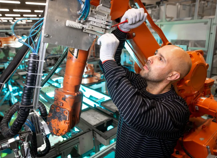 An industrial machinery mechanic or industrial maintenance technician does maintenance on an automatic robot arm in an auto factory
