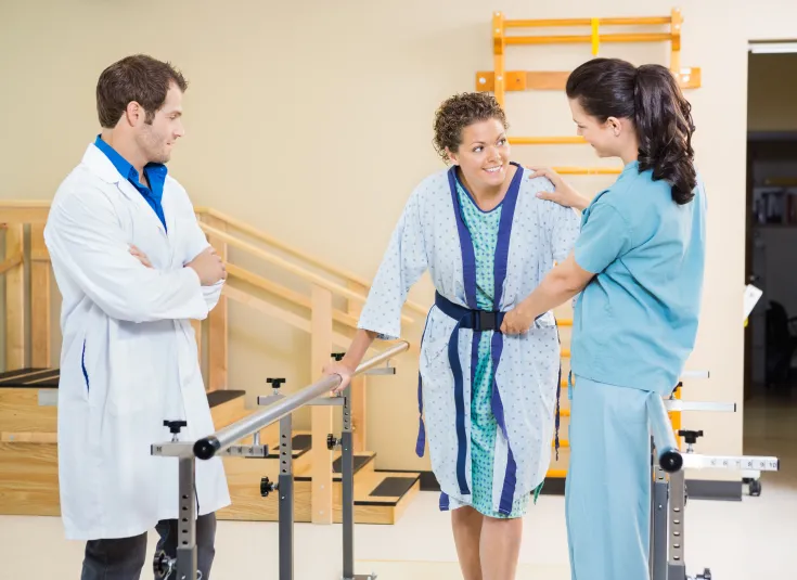 A physical therapy assistant helps a woman keep her balance as she tries to walk in the hospital