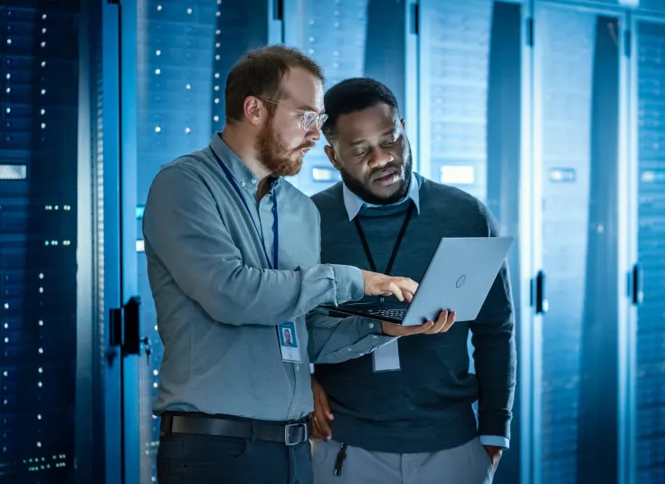 Two systems analysts in front of a bank of servers, keeping computer systems running efficiently