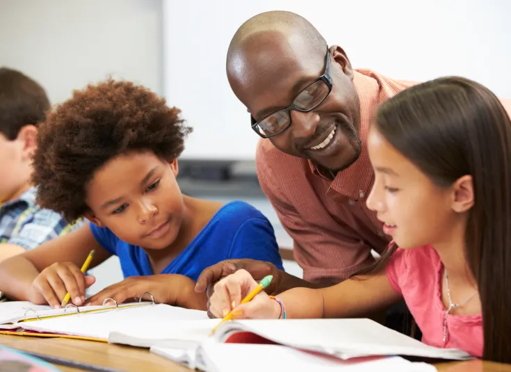 A teacher assistant helps two students with classwork