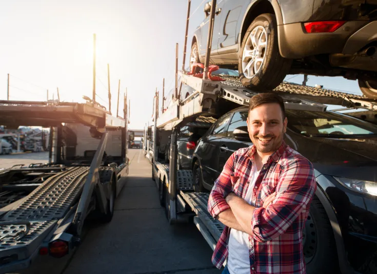 Truck driver stands in front of cars he is transporting to a dealership