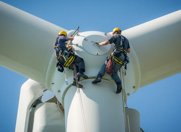 Wind turbine technicians inspect a turbine at a wind farm