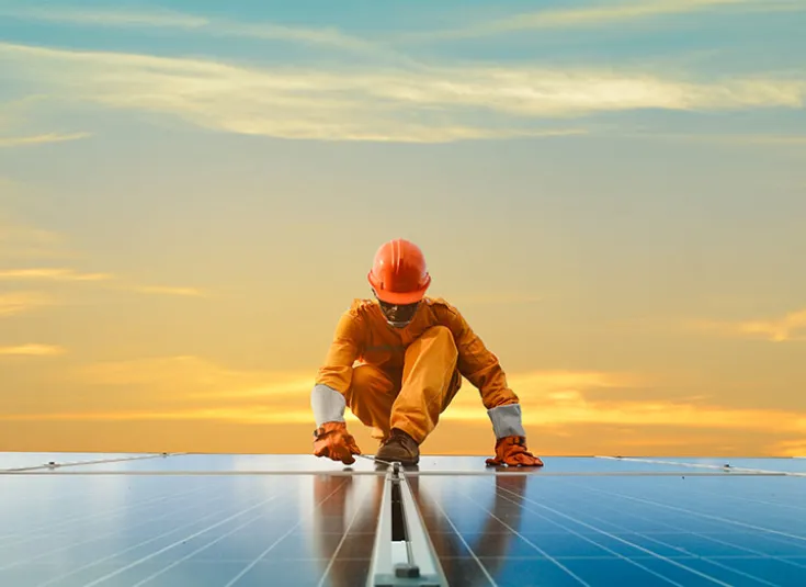 A solar technician installs solar panels with a sunset in the background