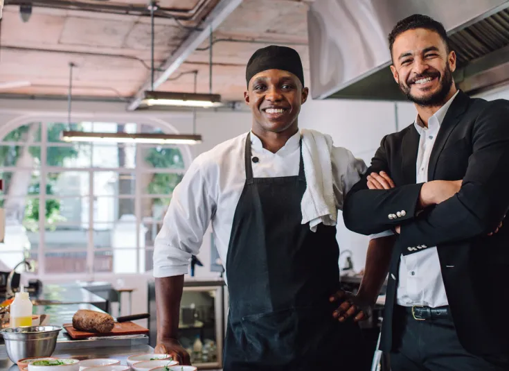 Black male kitchen manager smiles with the restaurant manager in the kitchen