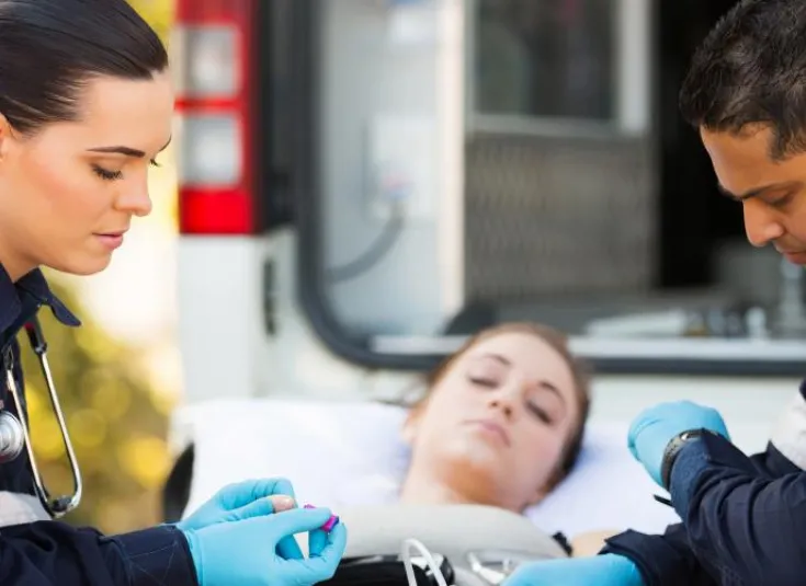 paramedics stabilize a female patient on a gurney in front of an ambulance