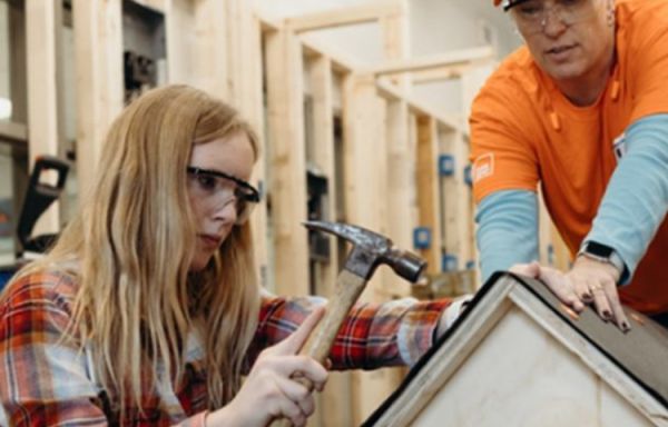 Woman uses a hammer in a residential construction site with support from a man in a Home Depot shirt