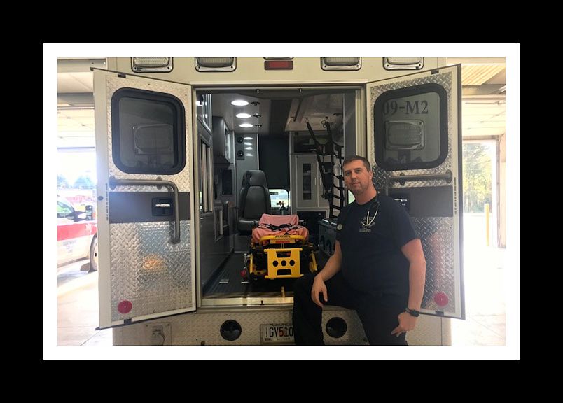 Paramedic Ryan Hollingsworth stands in front of the open back doors of an ambulance