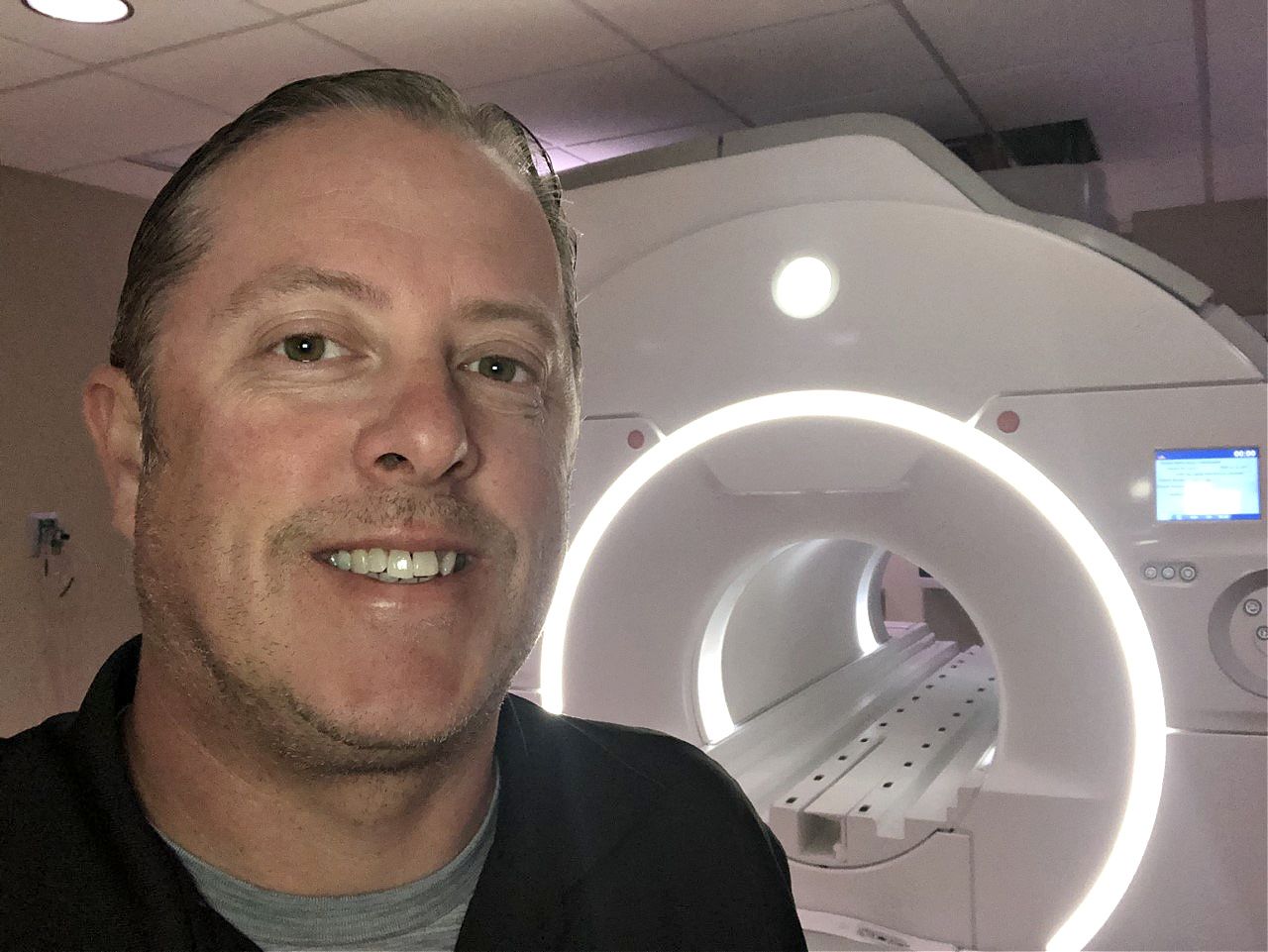 Joe Seibert, MRI technician, stands in front of an MRI machine