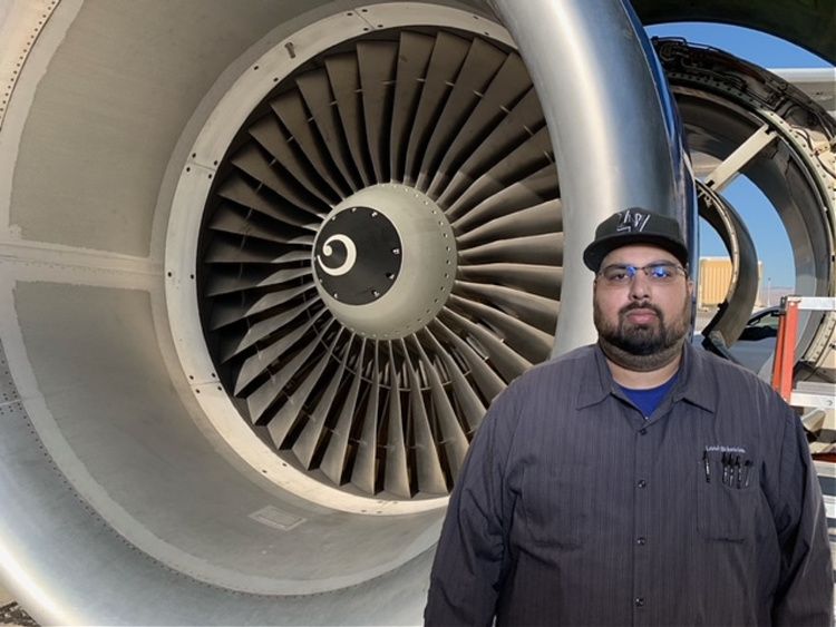 Aircraft Mechanic Lorenzo Carlos Perez stands in front of an airplane engine.