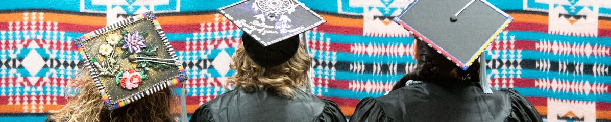 Three graduates in cap and gown looking at tapestry