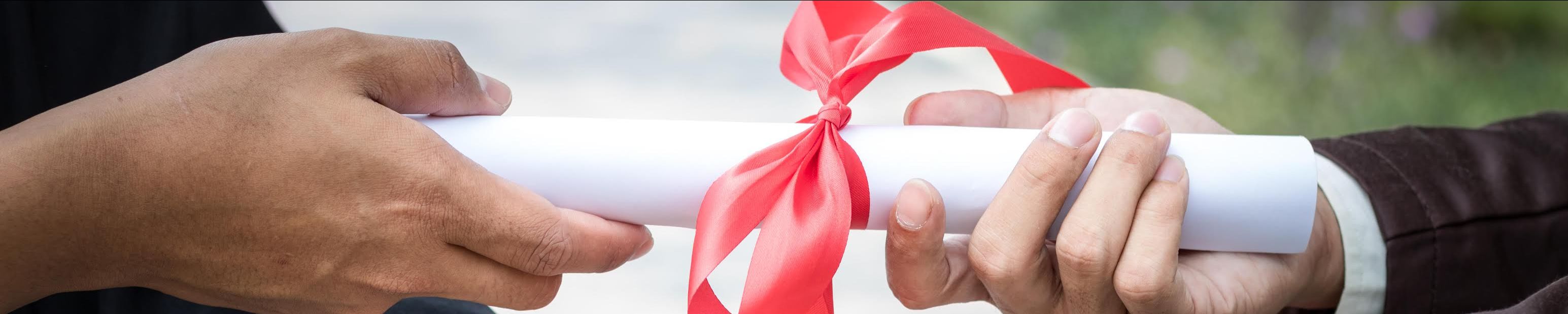 Two hands holding a diploma wrapped in a red ribbon