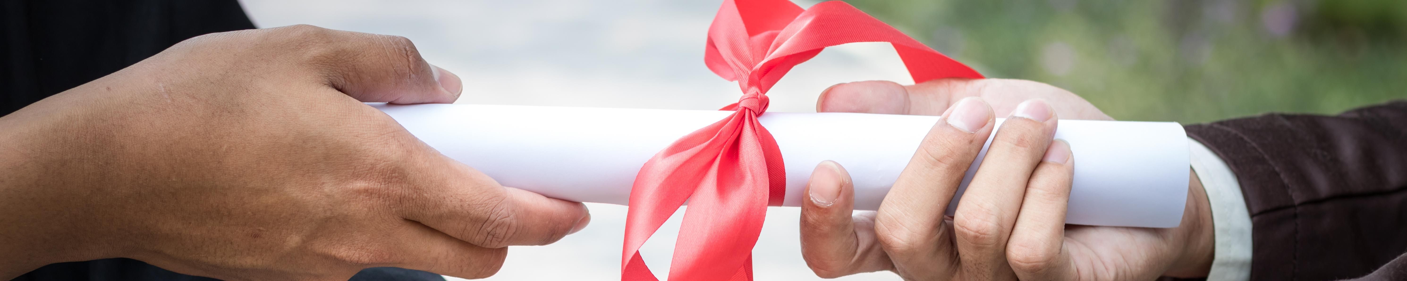 A photo of two hands holding either side of a diploma wrapped in a red bow.