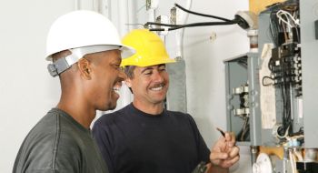 Two electricians work on an electrical panel. Electricians are among the good paying jobs that don't require a degree