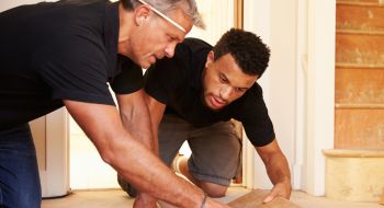 Two men work on flooring, example of on the job training