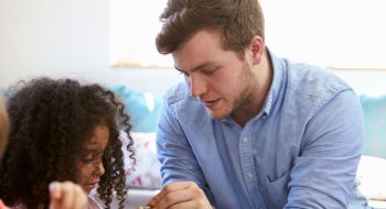 Young male preschool teacher works with a child to solve a puzzle. Example of associate degree jobs that may surprise you.