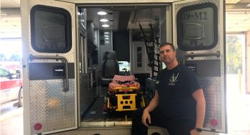 Paramedic Ryan Hollingsworth in front of the open doors of an ambulance