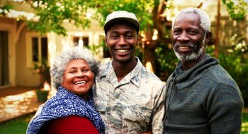black soldier stands with proud parents in front of a house