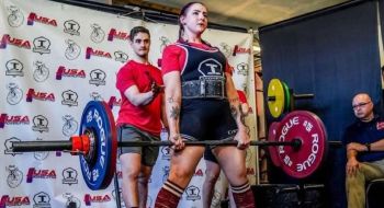 A woman weightlifter stands holding a straight bar with weights on either end.