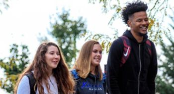 Three students walk together through campus on a bright autumn day.