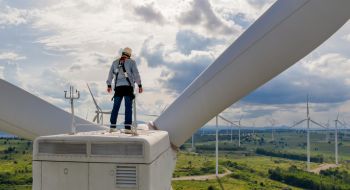 Wind turbine technician stands on the nacelle at the top of a wind turbine