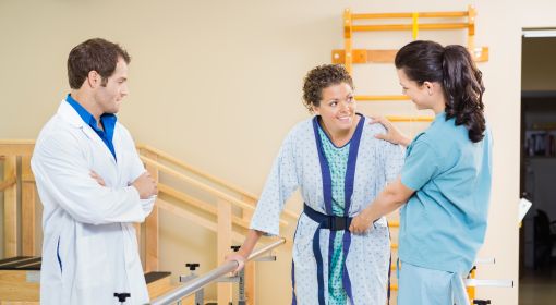 A physical therapy assistant helps a woman keep her balance as she tries to walk in the hospital