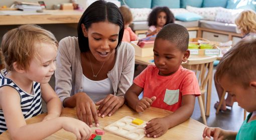 A black female preschool teacher helps three preschool students learn their shapes
