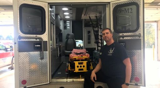 Paramedic Ryan Hollingsworth in front of the open doors of an ambulance