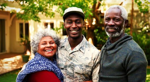 black soldier stands with proud parents in front of a house