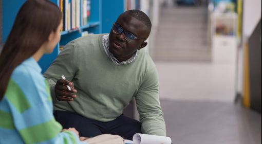 A Black male counselor talks with a female student with long, black hair and a colorful striped sweater