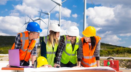 4 wind turbine technicians look over work plans with wind turbines behind them