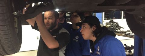 Auto mechanic Jake Sorenson shows two technicians how to fix something on a car