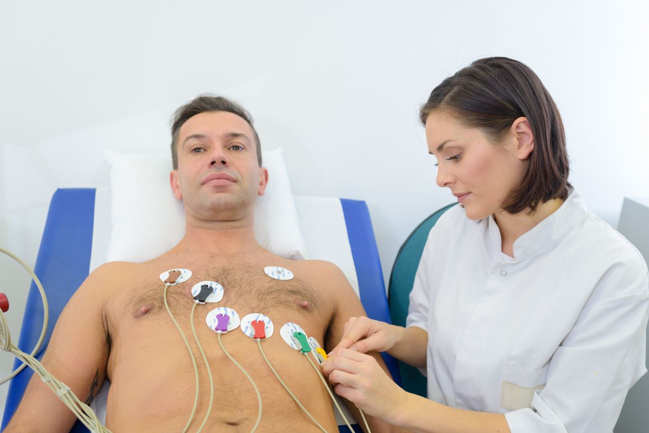 Female cardiovascular technician applies cardiogram electrodes on a male patient’s chest for an EKG