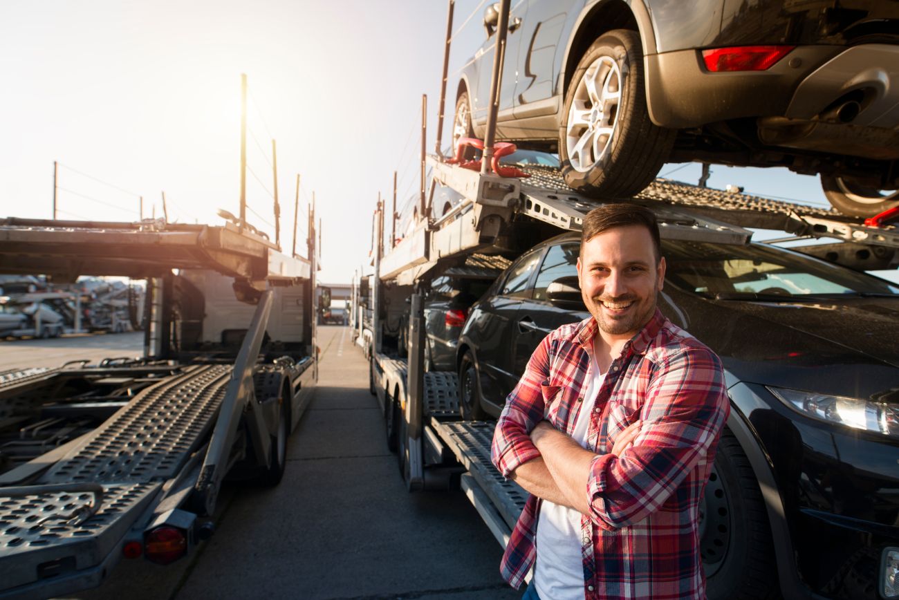 Truck driver stands in front of cars he is transporting to a dealership