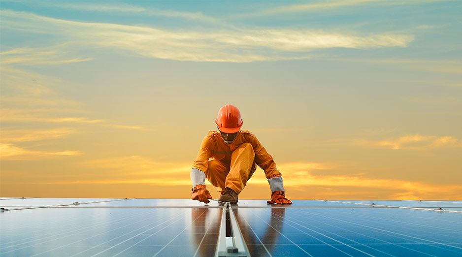 A solar technician installs solar panels with a sunset in the background
